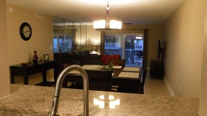 A kitchen with granite countertops, a stainless steel sink, a dining area with a table and chairs, a sofa, and a balcony with a view. - Top floor Ocean View Cocoa Beach Condo at the Spanish Main (Cocoa Beach)