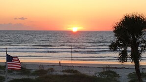 A sunset over the ocean with a flag, a palm tree, and a pathway. - Top floor Ocean View Cocoa Beach Condo at the Spanish Main (Cocoa Beach)