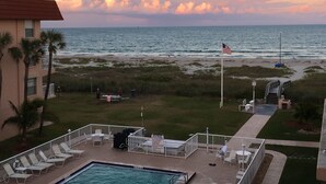 A pool area with lounge chairs, a flag, and a view of the beach and ocean. - Top floor Ocean View Cocoa Beach Condo at the Spanish Main (Cocoa Beach)