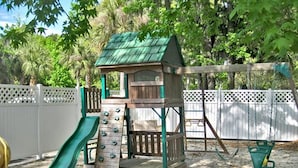 A playground with a slide, climbing wall, and a small house-like structure.