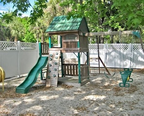 Un parque infantil con un tobogán, una pared de escalada y una casita.