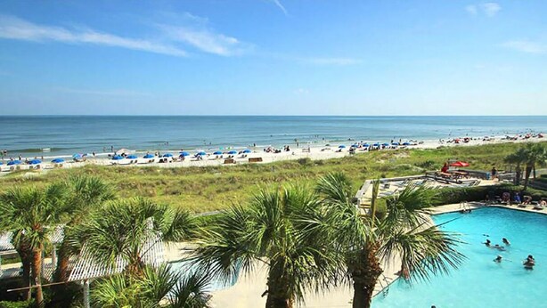 A beach resort with a swimming pool, beach umbrellas, and palm trees.