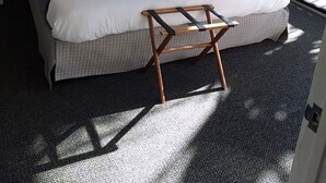 A neatly made bed with a blue and white bedspread, two framed pictures on the wall, a bedside lamp, and a wooden stool in front of the bed.