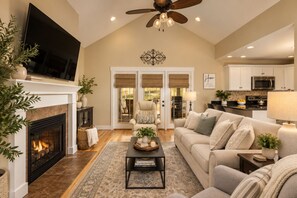 A spacious living room with a fireplace, a sofa set, a coffee table, and a television mounted on the wall.