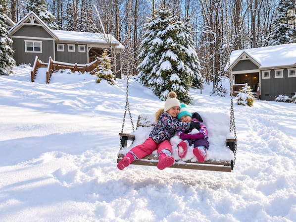 A wooden swing set in a snowy landscape with two people sitting on it.