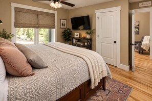 Quarto com cama, televisão, porta e janela com persianas.