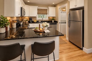 A modern kitchen with white cabinetry, a granite countertop, a stainless steel refrigerator, and a central island with bar stools.