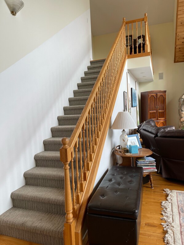 Una escalera con barandillas de madera que conduce a un piso superior, un sofá de cuero, una mesita con una lámpara y una estantería.