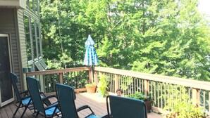 A wooden deck with four green chairs and a blue umbrella, surrounded by lush greenery. - big house on the private lake ,10 minutes to downtown and Lake Michigan (Traverse City)