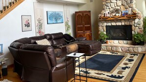A spacious living room with a brown leather sectional sofa, a stone fireplace, and a wooden staircase. - big house on the private lake ,10 minutes to downtown and Lake Michigan (Traverse City)