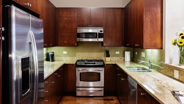 A modern kitchen with stainless steel appliances, wooden cabinets, and a green tiled backsplash. - Wrigley Field MVP Suite 1 Bedroom Apartment (Chicago)