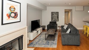 A modern living room with a flat-screen TV, grey sofa, coffee table, and a framed sports poster. - Wrigley Field MVP Suite 1 Bedroom Apartment (Chicago)