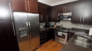 A modern kitchen with dark wooden cabinets, stainless steel appliances, a tiled backsplash, and a wooden floor. - Wrigley Field MVP Suite 1 Bedroom Apartment (Chicago)