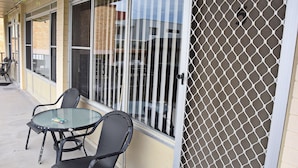 Un patio con un tavolo in vetro e due sedie, un cancello in metallo e un edificio sullo sfondo.