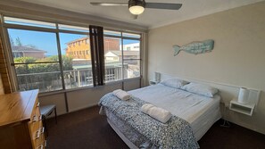 A bedroom with a large window, a ceiling fan, a bed with a patterned bedspread, and a wall-mounted fish decoration.
