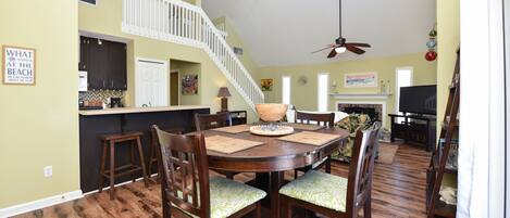 A spacious dining area with a high ceiling, a staircase, and a kitchen in the background.