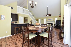 A spacious dining area with a high ceiling, a staircase, and a kitchen in the background. - AMAZING VIEW! Fun, Pets Welcome, Steps from Beach (St George Island)