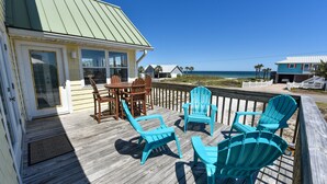 Une terrasse en bois agrémentée de chaises Adirondack turquoise, d’une table en bois et d’une porte vitrée donnant accès à un bâtiment doté d’un toit végétalisé.