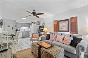 A living room with a grey sofa, two ottomans, a coffee table, and a dining area with a table and chairs.