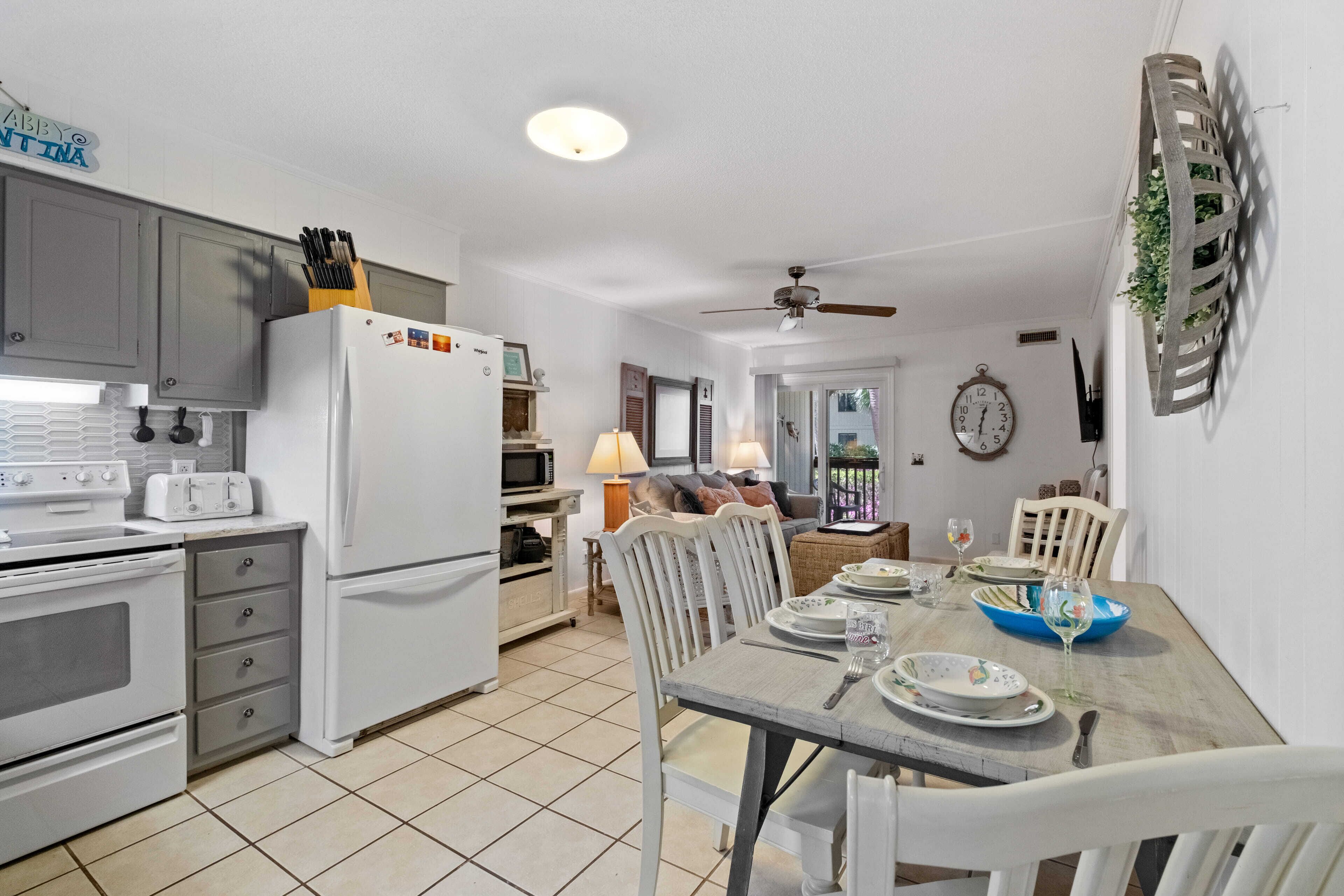 A modern kitchen with white appliances, grey cabinets, and a dining area with a wooden table set for four.