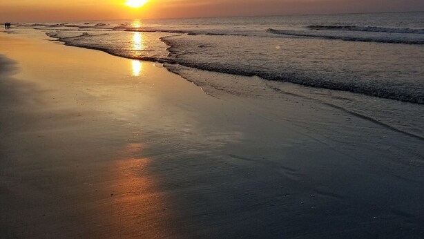 A beach at sunset with calm waves and a clear sky.
