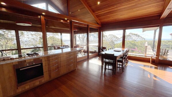 A modern kitchen with a large island, wooden flooring, and large windows offering a view of the outdoors.