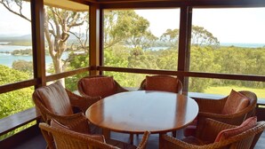 A covered outdoor seating area with wicker chairs and a round table, overlooking a scenic landscape with trees and a body of water. - Tallowood Southwest Rocks - Bring your own linen (South West Rocks)