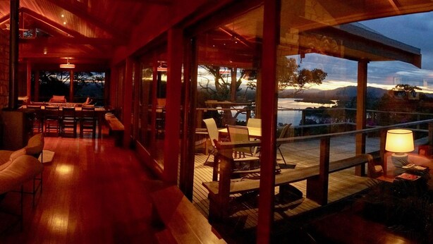 A spacious indoor area with a wooden floor, a dining area with tables and chairs, and large windows offering a view of the outdoors. - Tallowood Southwest Rocks - Bring your own linen (South West Rocks)