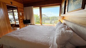 A room with a bed, a television, and a window with a view of trees and mountains.