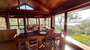A wooden dining area with a table and chairs, large windows offering a view of the outdoors.