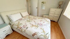 A bedroom with a floral bedspread, a bedside table, a dresser, and a mirror.