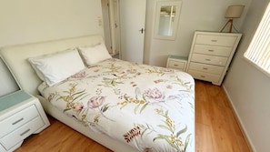 A bedroom with a floral bedspread, a bedside table, a dresser, and a mirror.