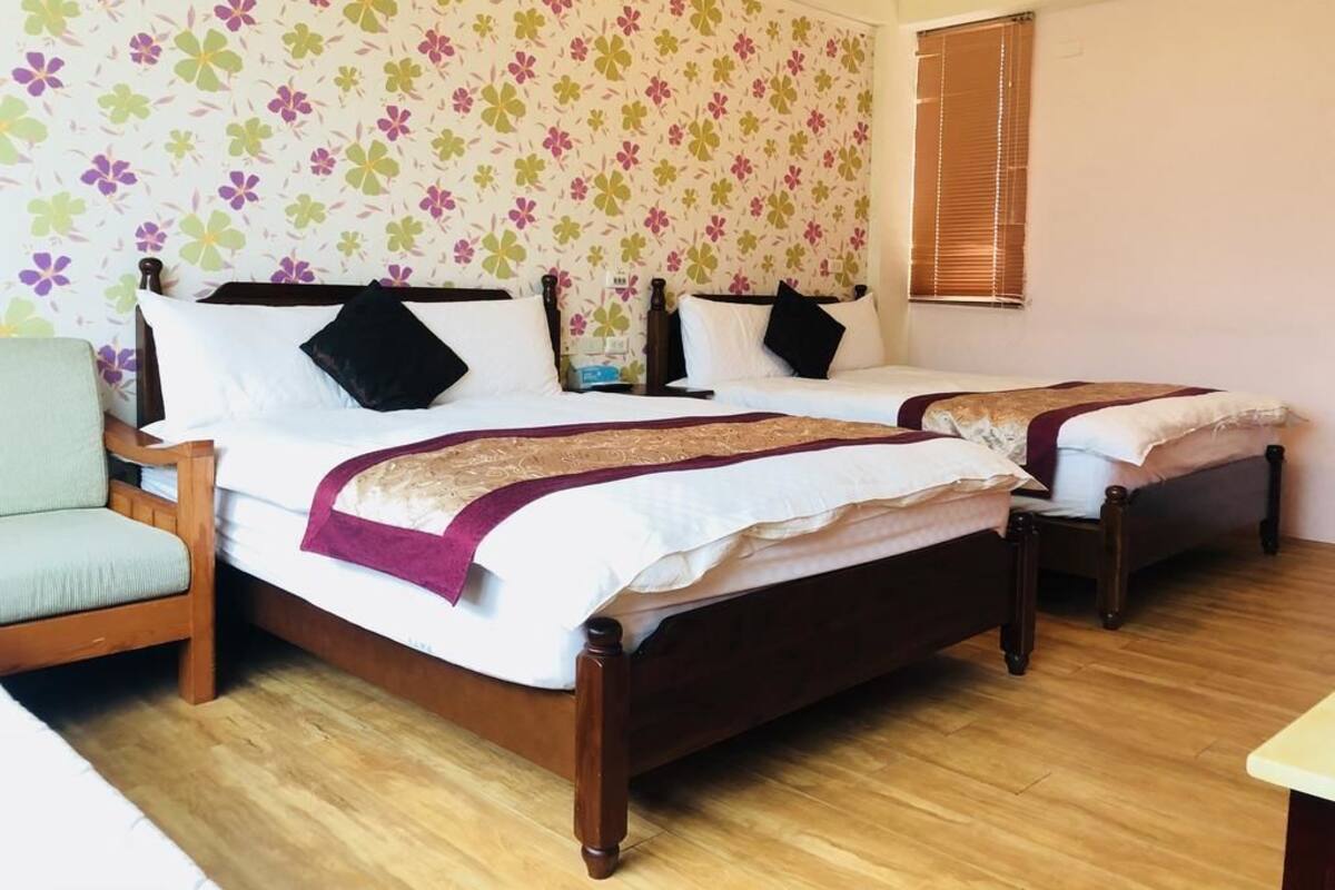 A hotel room with two wooden beds, a wooden chair, and a floral wallpaper.