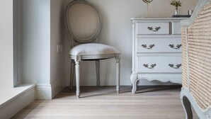 A room with a high ceiling, a large mirror, a chair, a dresser, and a wicker chair. - Shrubbery Mews 5 * Apt 2 (Kenmare)