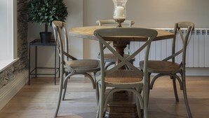 A dining area with a round table, four chairs, a hanging pendant light, a potted plant, a framed picture on the wall, and a radiator. - Shrubbery Mews 5 * Apt 2 (Kenmare)
