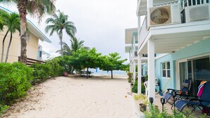Une propriété située en bord de mer, dotée d’un chemin piétonnier de sable, de palmiers et d’un patio couvert avec des sièges extérieurs.