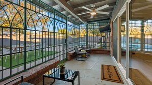 A covered patio area with a view of a garden and a brick wall. There are outdoor seating arrangements and a ceiling fan. - Lester Place: Retro-Inspired Artist’s Escape with Pool! (Tucson)