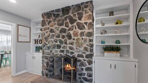 A modern living room with a stone fireplace, white cabinetry, and a decorative shelf with various items. - Lester Place: Retro-Inspired Artist’s Escape with Pool! (Tucson)