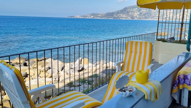 A balcony with yellow-striped chairs, a table with a yellow tablecloth, and a view of the sea. - THE FISHERMAN'S HOUSE (Ospedaletti)