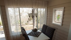 A dining area with a table and chairs, a chandelier, a window with a view of the outdoors, and a decorative window frame.