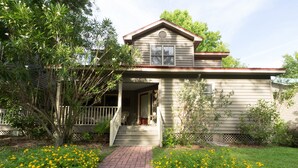 A two-story house with a front porch, a small garden with yellow flowers, and a wooden fence.
