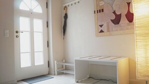 Un couloir avec une porte blanche, un porte-manteau avec un parapluie, un bureau blanc et un mur orné d’un tableau aux motifs géométriques.