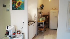 Une cuisine compacte équipée d’une machine à café, d’un réfrigérateur et ornée d’un tableau représentant des tournesols.