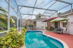 Une piscine avec un patio couvert, du mobilier d’extérieur et une vue sur la maison en arrière-plan.
