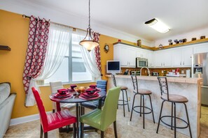 Une cuisine moderne avec des meubles blancs, un coin repas avec des chaises rouges et vertes, et un bar avec des tabourets.