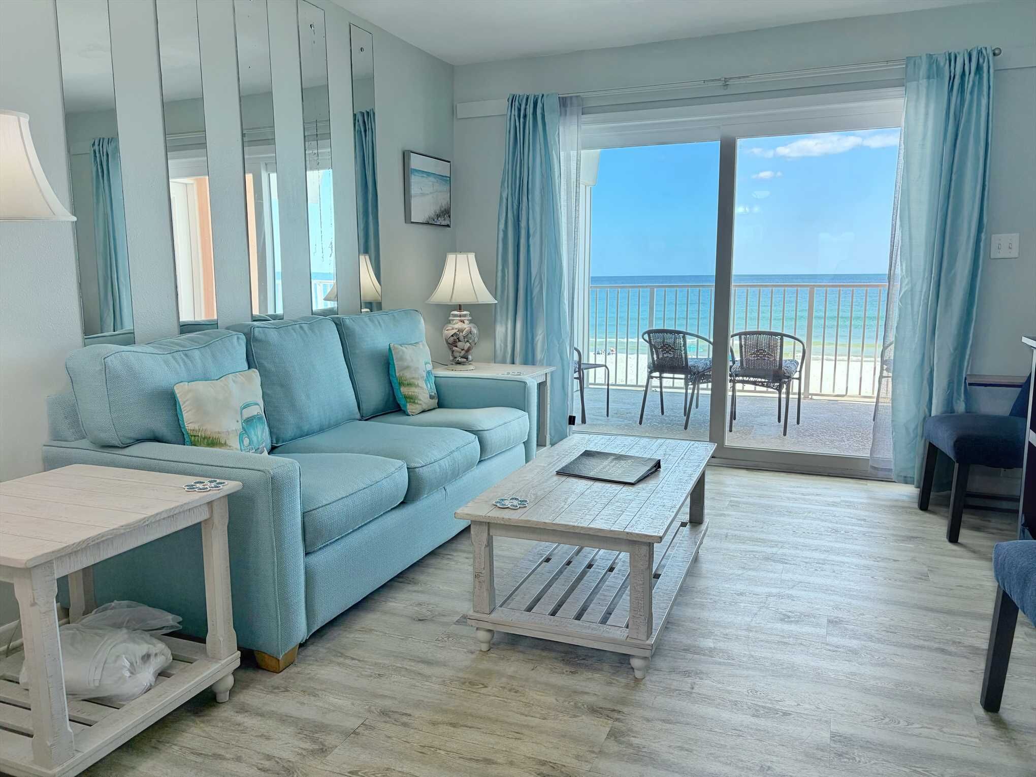A living room with a sofa, coffee table, and chairs, a balcony with a view of the beach.