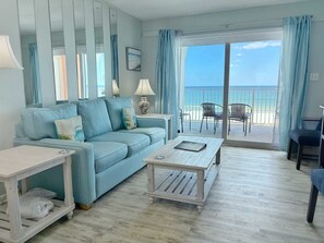 Un salón con sofá, mesa de centro y sillas, un balcón con vista a la playa.