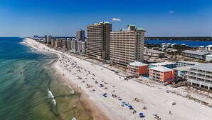 A coastal hotel with multiple floors, beachfront location, and a sandy beach with umbrellas.