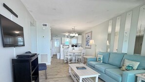 A living room with a TV, a sofa, a coffee table, and a dining area with chairs and a table.