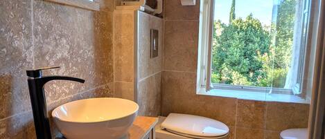A bathroom with a large white sink, a toilet, and a window with a view of greenery.